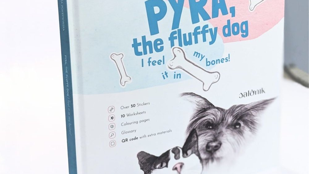 Książka "Pyra the fluffy dog" z widoczną okładką, na której są narysowane ołówkiem wizerunki kudłatego pieska i biało-czarnego kotka. Poza tytułem widnieje też hasło "I feel it in my bones!"