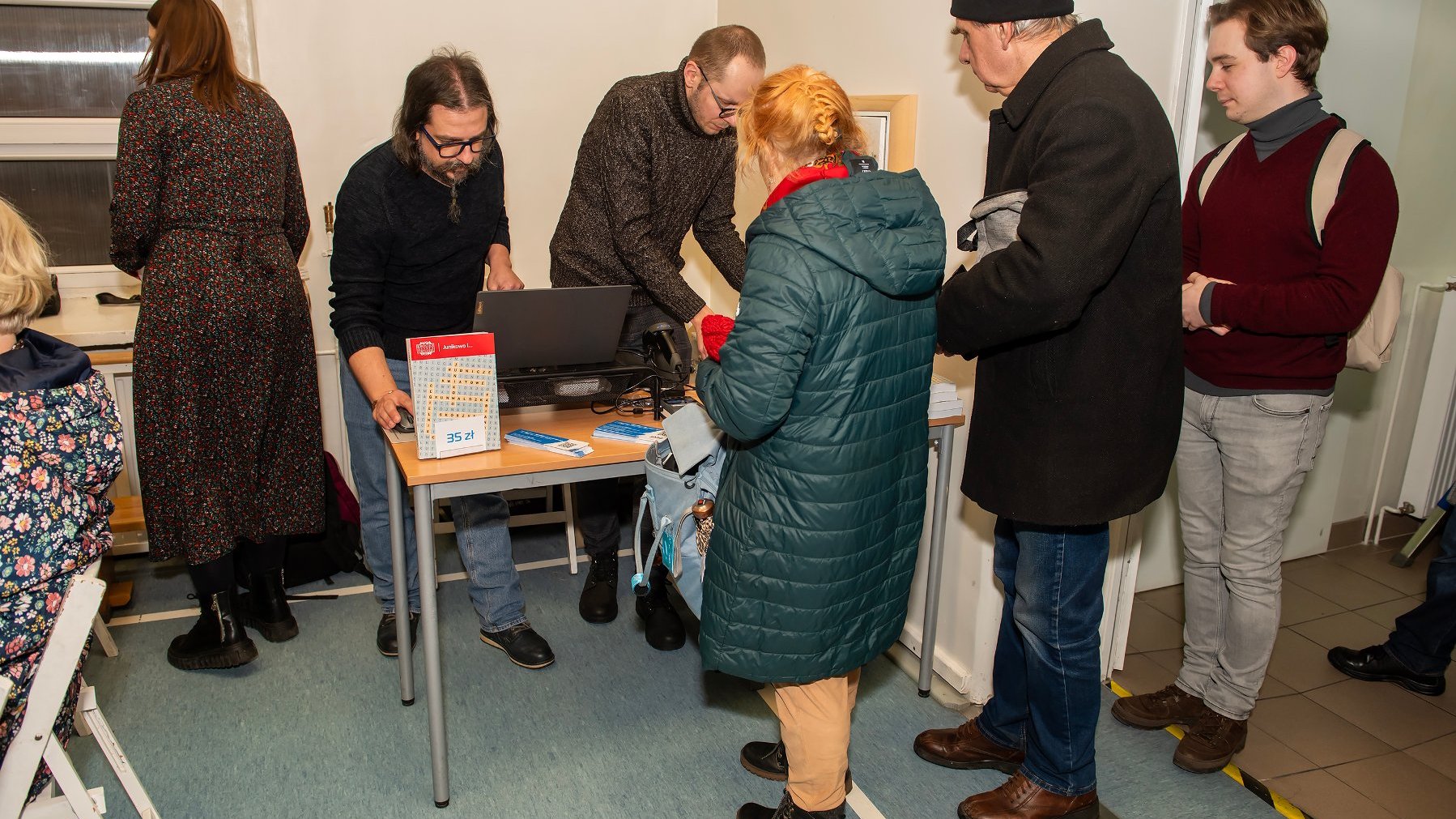 Sprzedaż książki podczas promocji. Dwóch mężczyzn sprzedaje książki ludziom stojącym w kolejce.