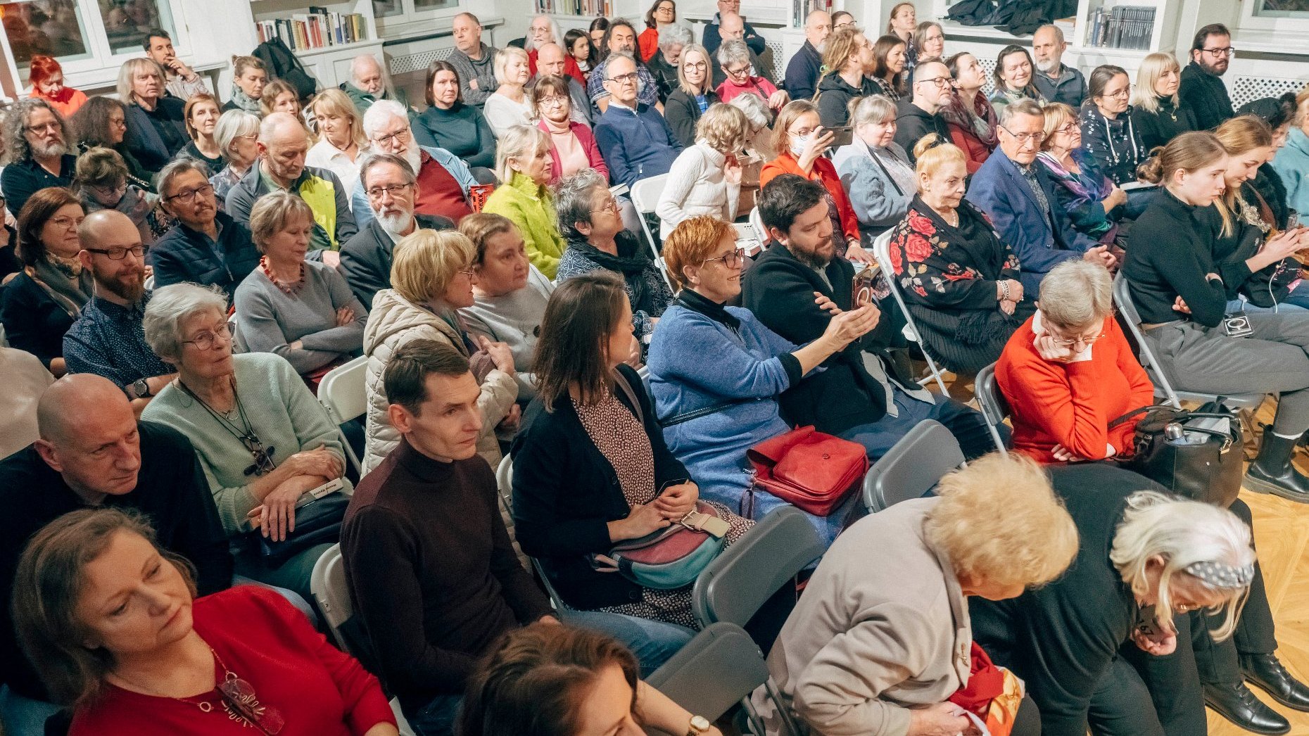 Licznie zgromadzona publiczność. Kilkadziesiąt ludzi siedzących na krzesłach.