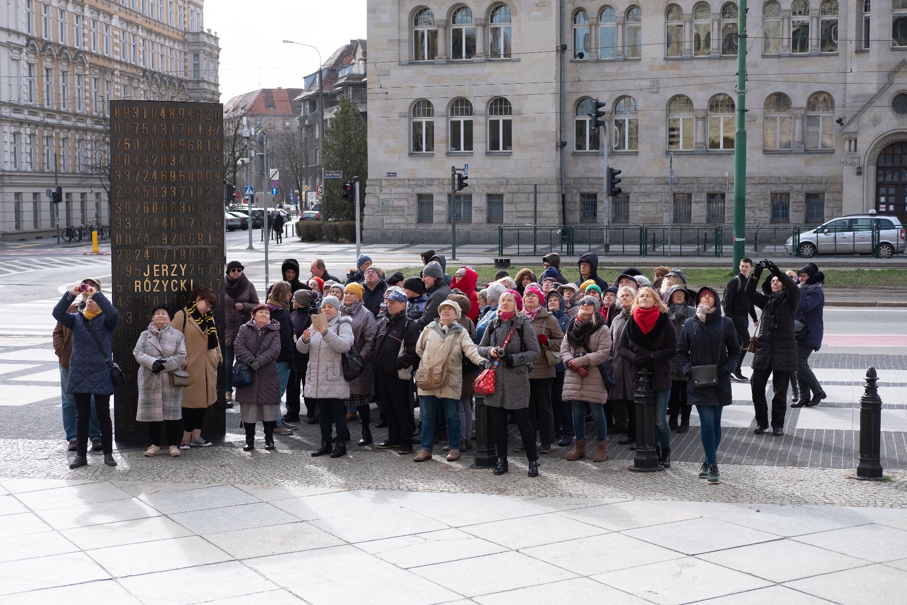 Zdjęcie przedstawia grupę ludzi stojących na chodniku - grafika artykułu