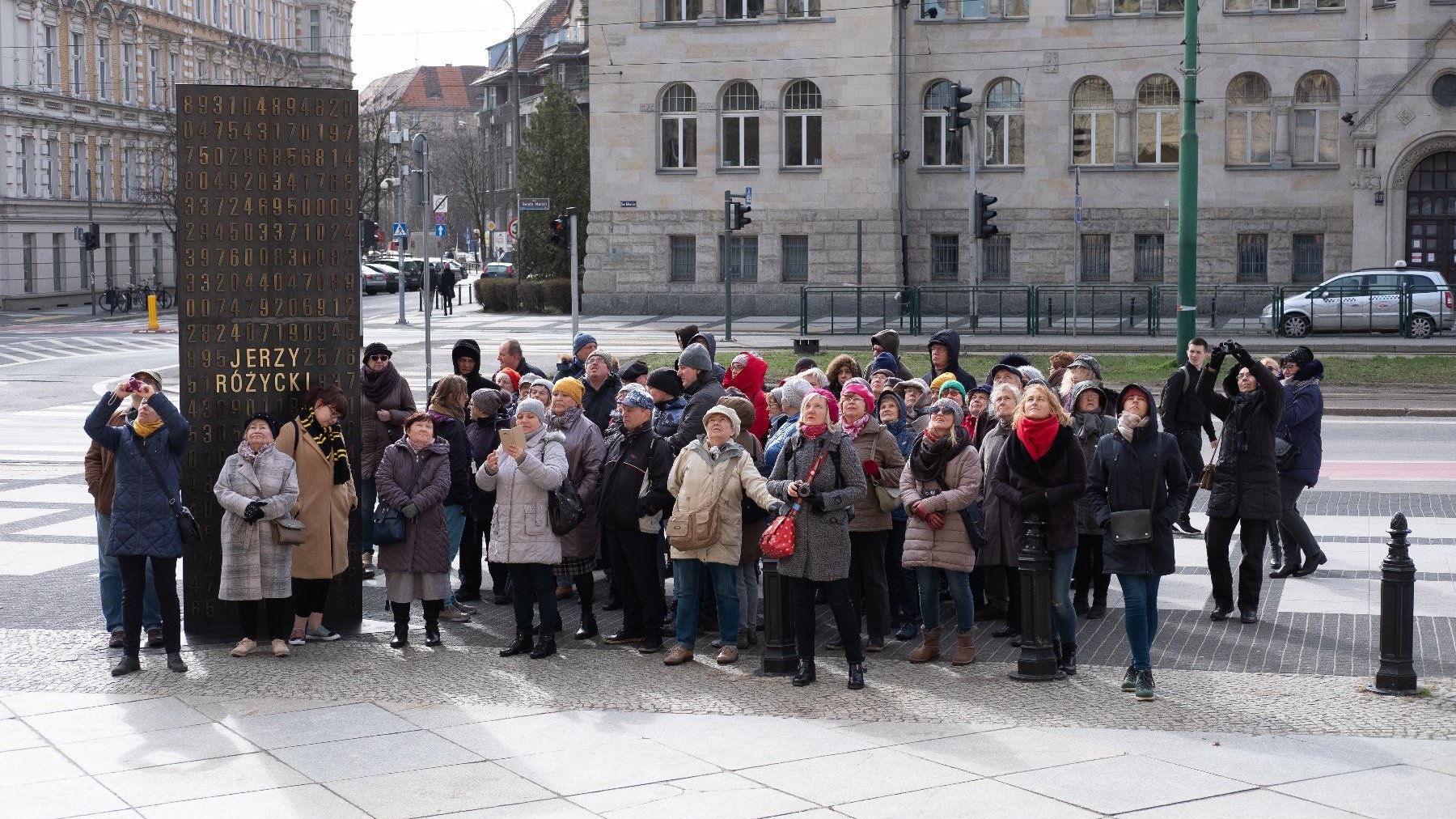 Zdjęcie przedstawia grupę ludzi stojących na chodniku