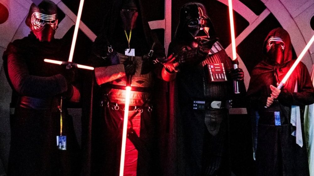 Cztery postacie znane z uniewersum "Star Wars" pozują w czarnych kostiumach, trzymając świecące miecze świetlne.