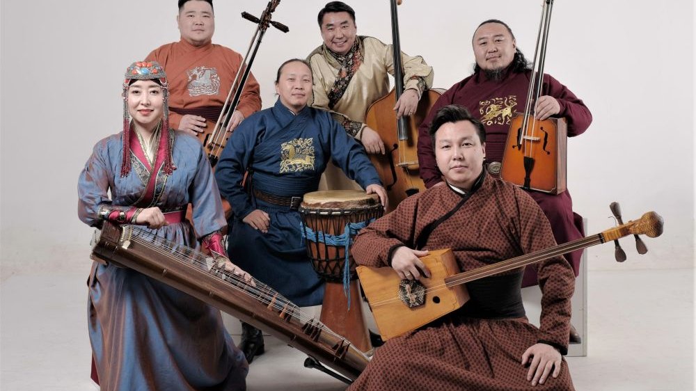 Pięcioro mężczyzn i jedna kobieta w tradycyjnych mongolskich strojach ludowych pozują z instrumentami.