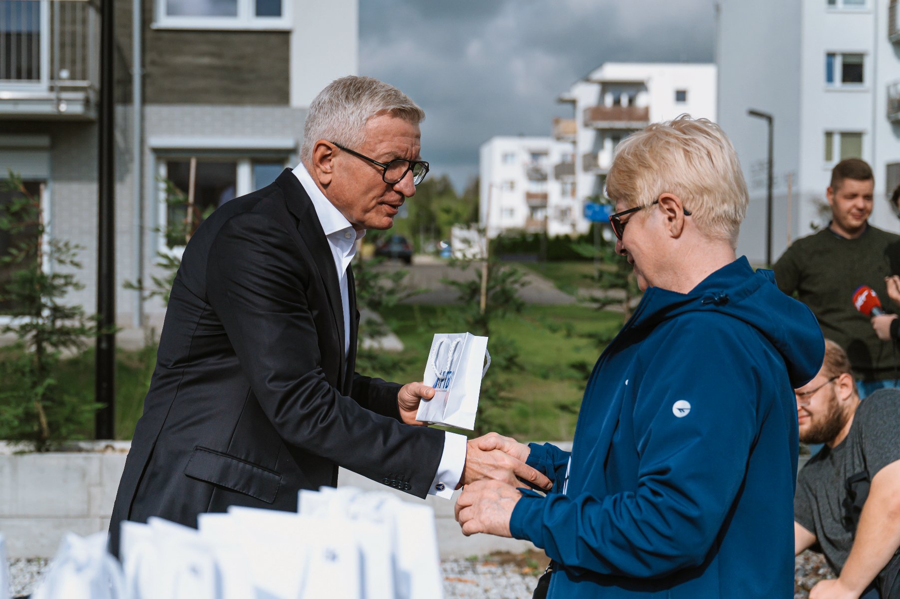 Na zdjęciu widać kobietę odbierającą klucze z rąk Prezydenta Poznania. Kobieta i Prezydent podają sobie rękę. W tle zdjęcia widać budynki mieszkalne. - grafika artykułu