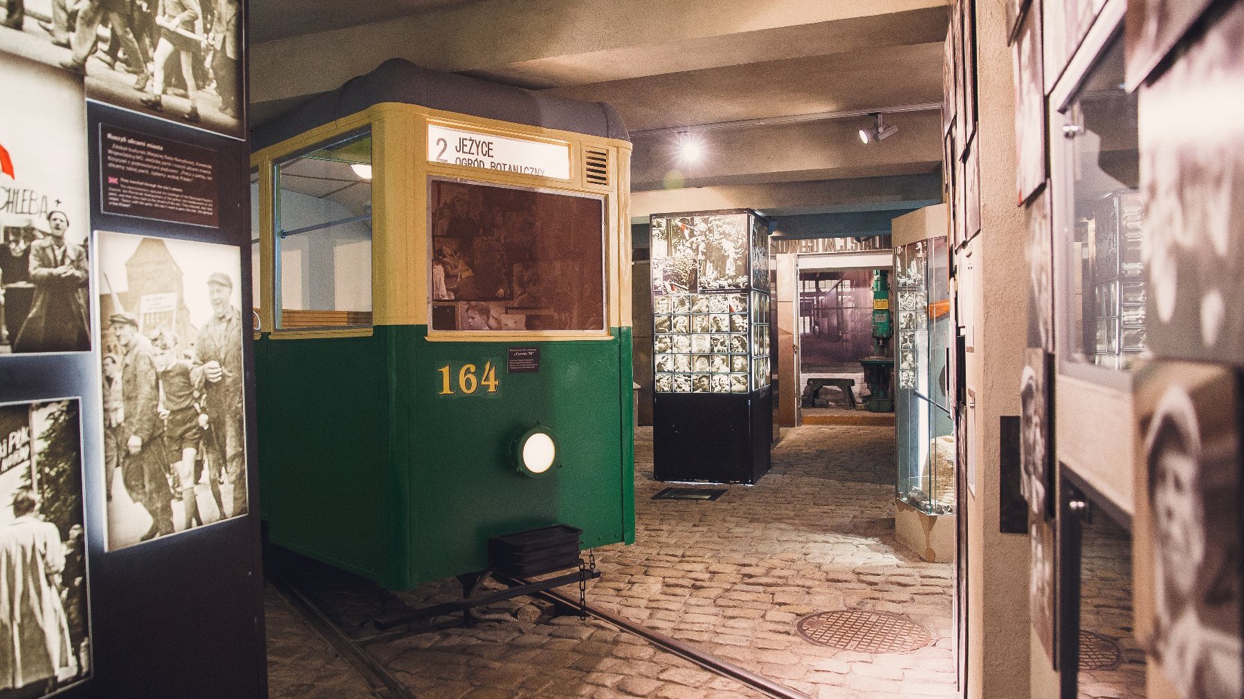 Część ekspozycji muzealnej Poznańskiego Czerwca 1956. W centrum stoi stary, żółto-zielony tramwaj z tablicą "2 Jeżyce. Ogród Botaniczny". Wokół tramwaju stoją filary ze zdjęciami z Poznańskiego Czerwca.