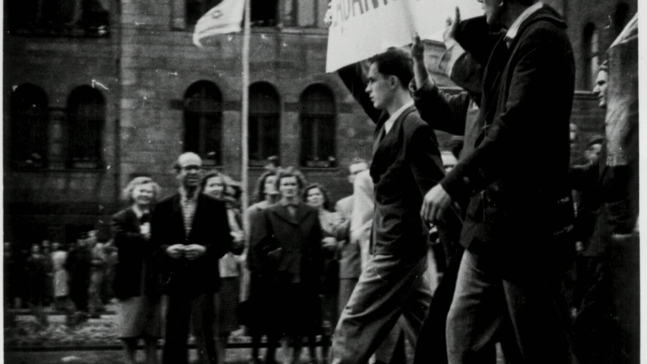 Widok z boku na pochód robotników. Na czele Janusz Kulas (pierwszy) z innymi dwoma mężczyznami niesie transparent "Żądamy chleba".