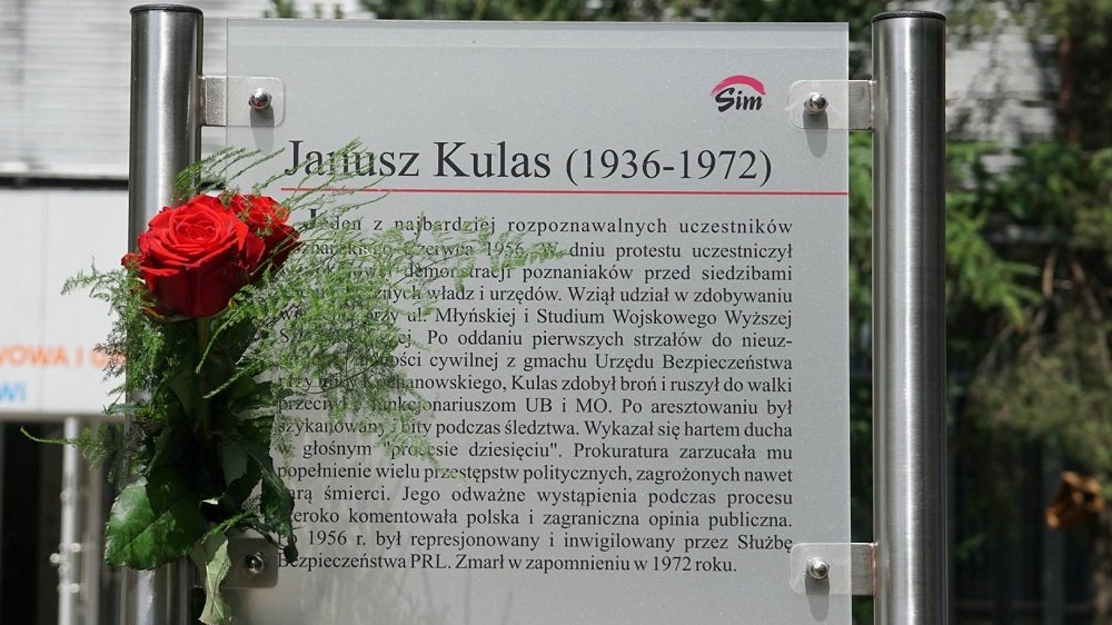Tablica upamiętniająca Janusza Kulasa. Na tablicy znajduje się biogram Kulasa. Przy tablicy zawieszono różę.