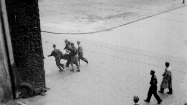Ulica Kochanowskiego 28 czerwca 1956 roku około godziny 12.30. Pięciu ludzi niesie rannego mężczyznę do szpitala przy ul. Mickiewicza.