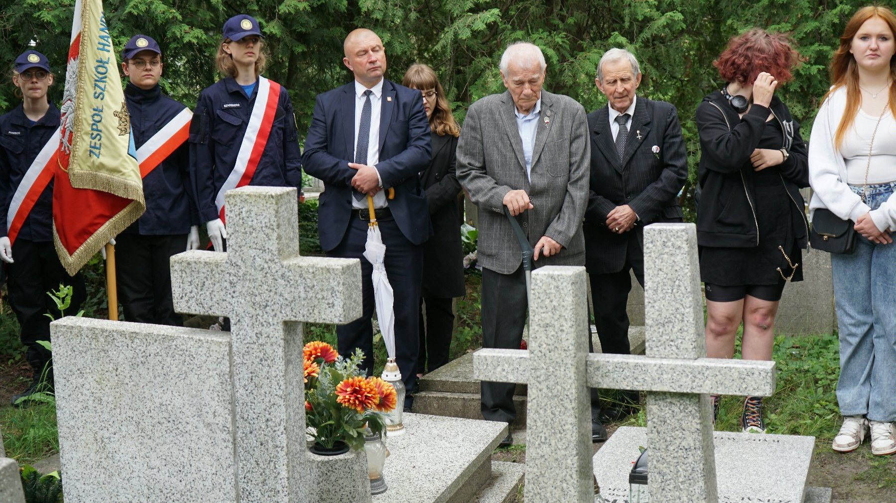 Zdjęcie przedstawia ludzi stojących przed grobami.