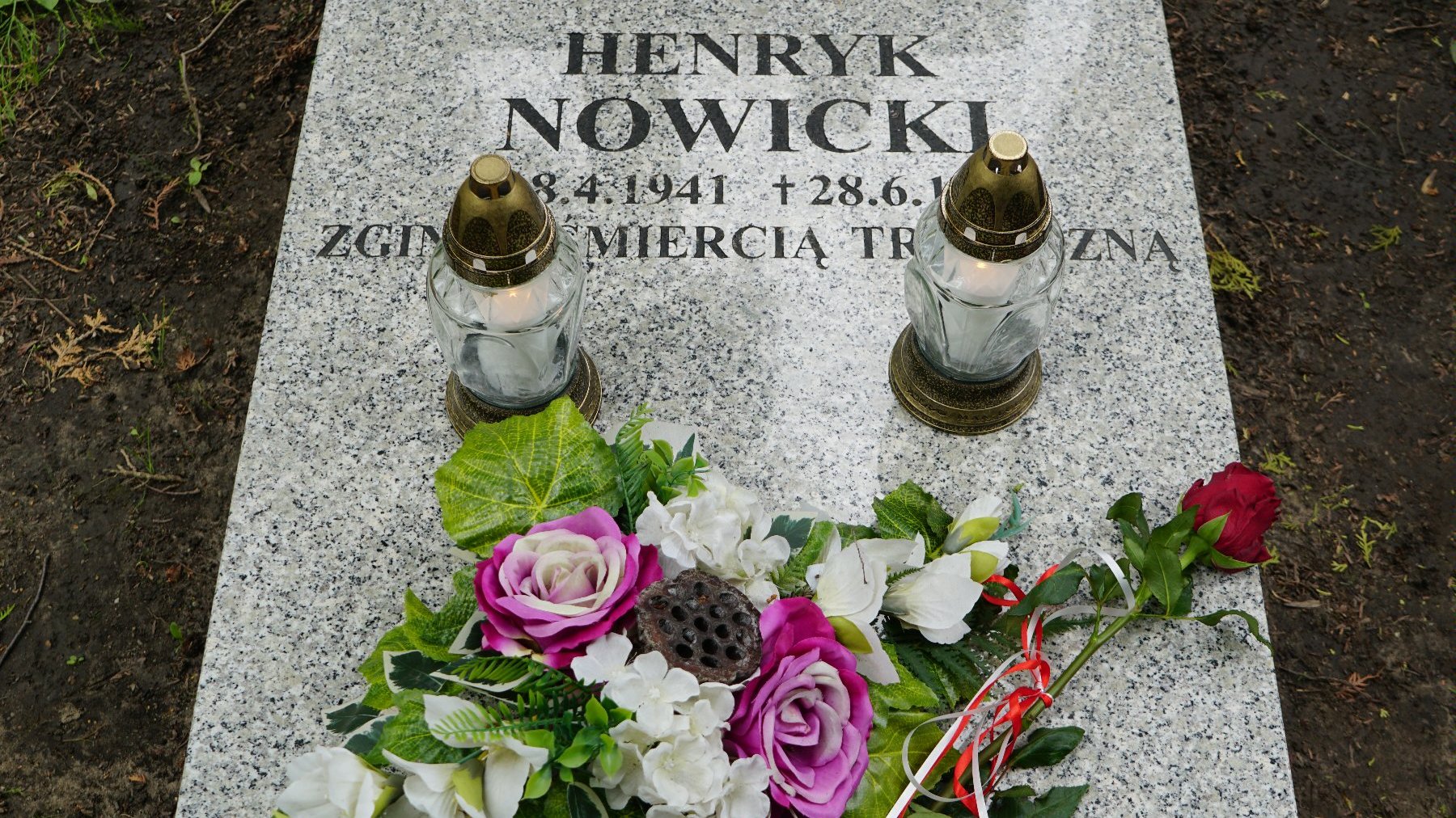 Zdjęcie przedstawia grób, na którym leżą kwiaty i znicz.