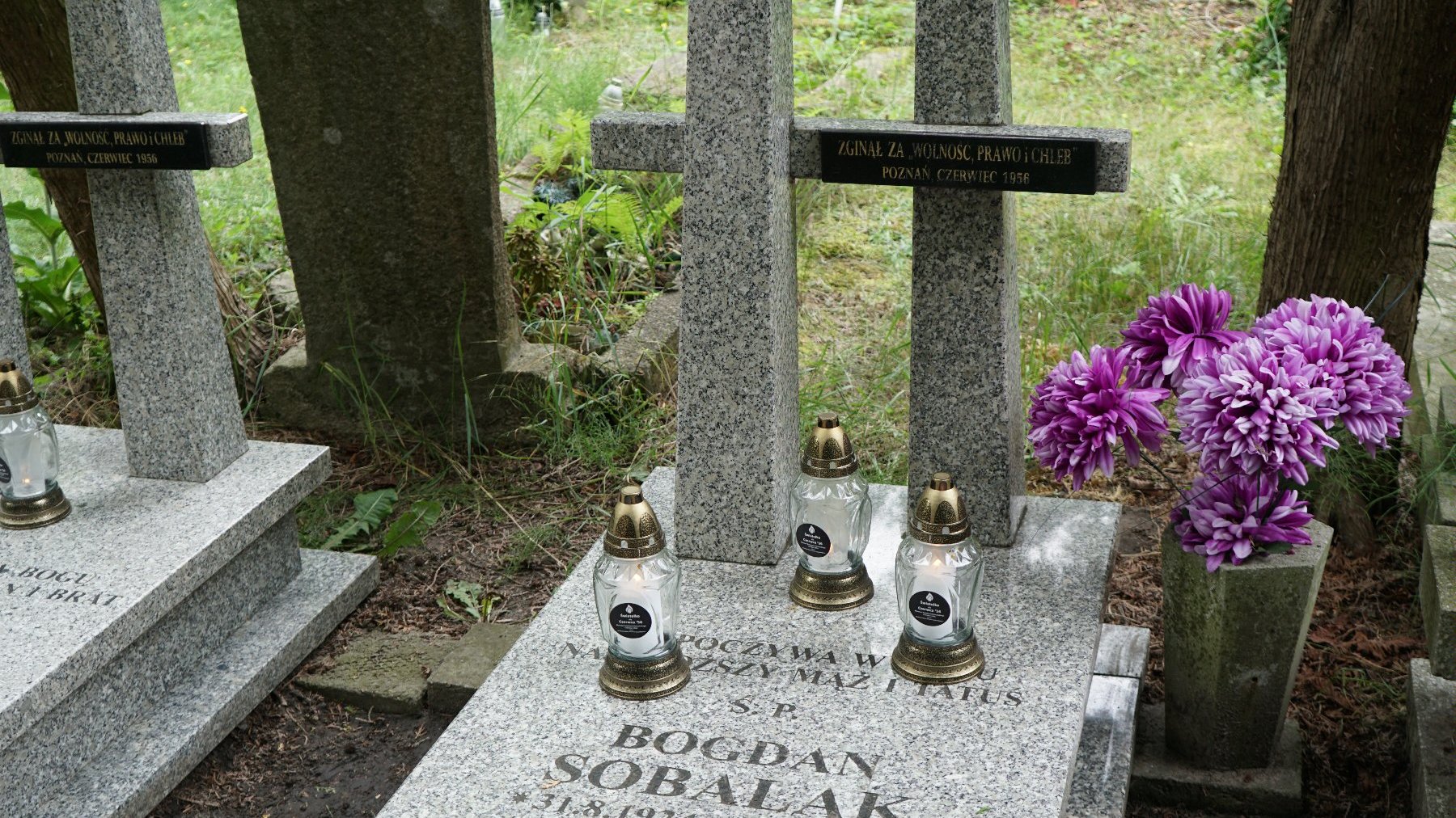 Zdjęcie przedstawia grób, na którym stoją znicze.