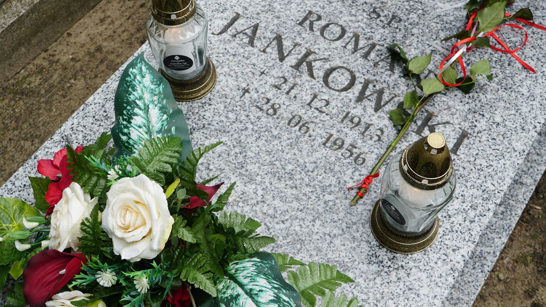 Zdjęcie przedstawia grób, na którym leżą kwiaty i znicze.