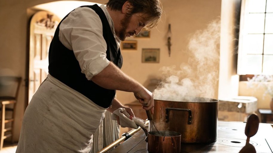 Zdjęcie, kadr filmu Bulion i inne namiętności, aktor stoi przed piecem kuchennym, z wielkiego garnka bucha para.