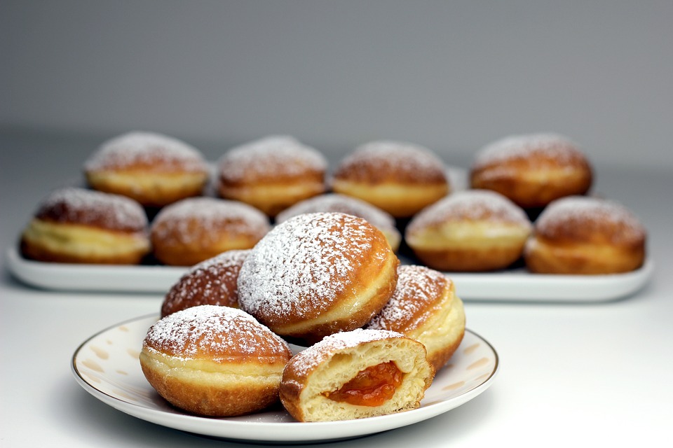 Pączki posypane cukrem pudrem. Jeden z nich jest przecięty na pół i wypływ z niego marmolada. - grafika artykułu