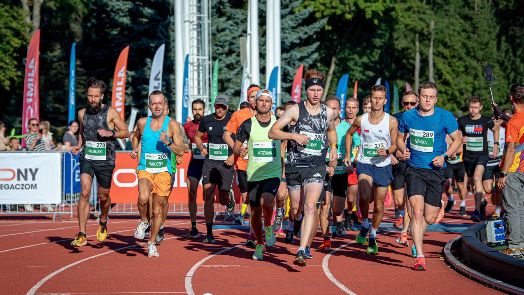 Grupa mężczyzn ubrana na sportowo rozpoczyna bieg na torze sportowym.