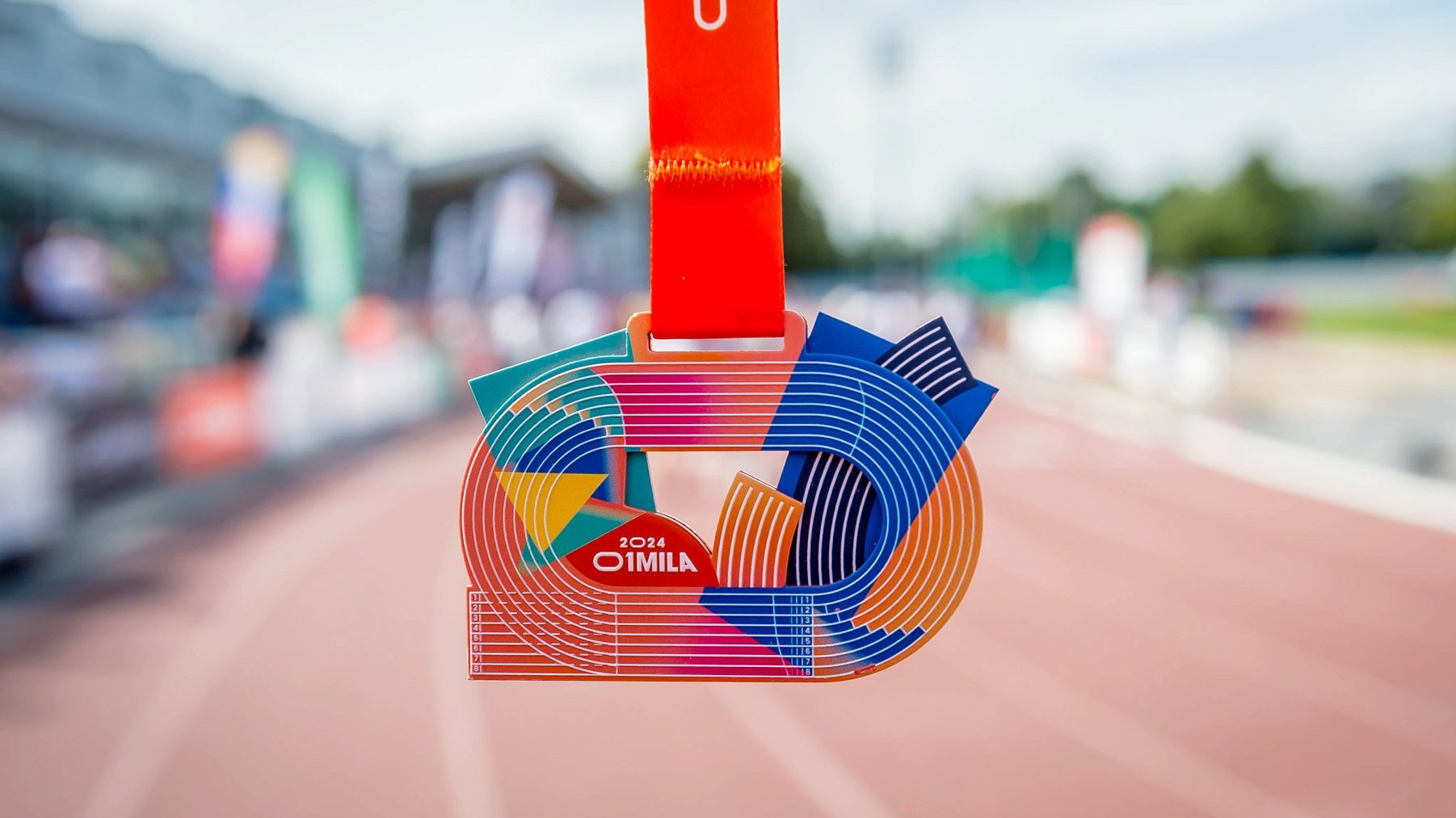 Zbliżenie na medal, który otrzymują uczestnicy po skonczeniu biegu. Medal przypomina tor atletyczny.