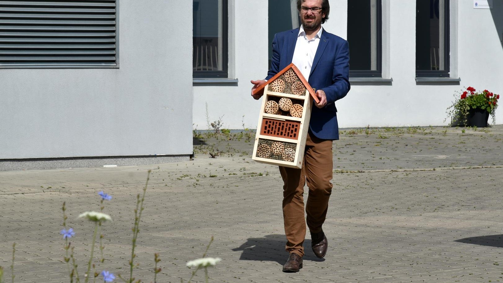 Krzysztof Albiński, dyrektor POSUM, niesie w ręku dom dla owadów. W tle - budynek POSUM.