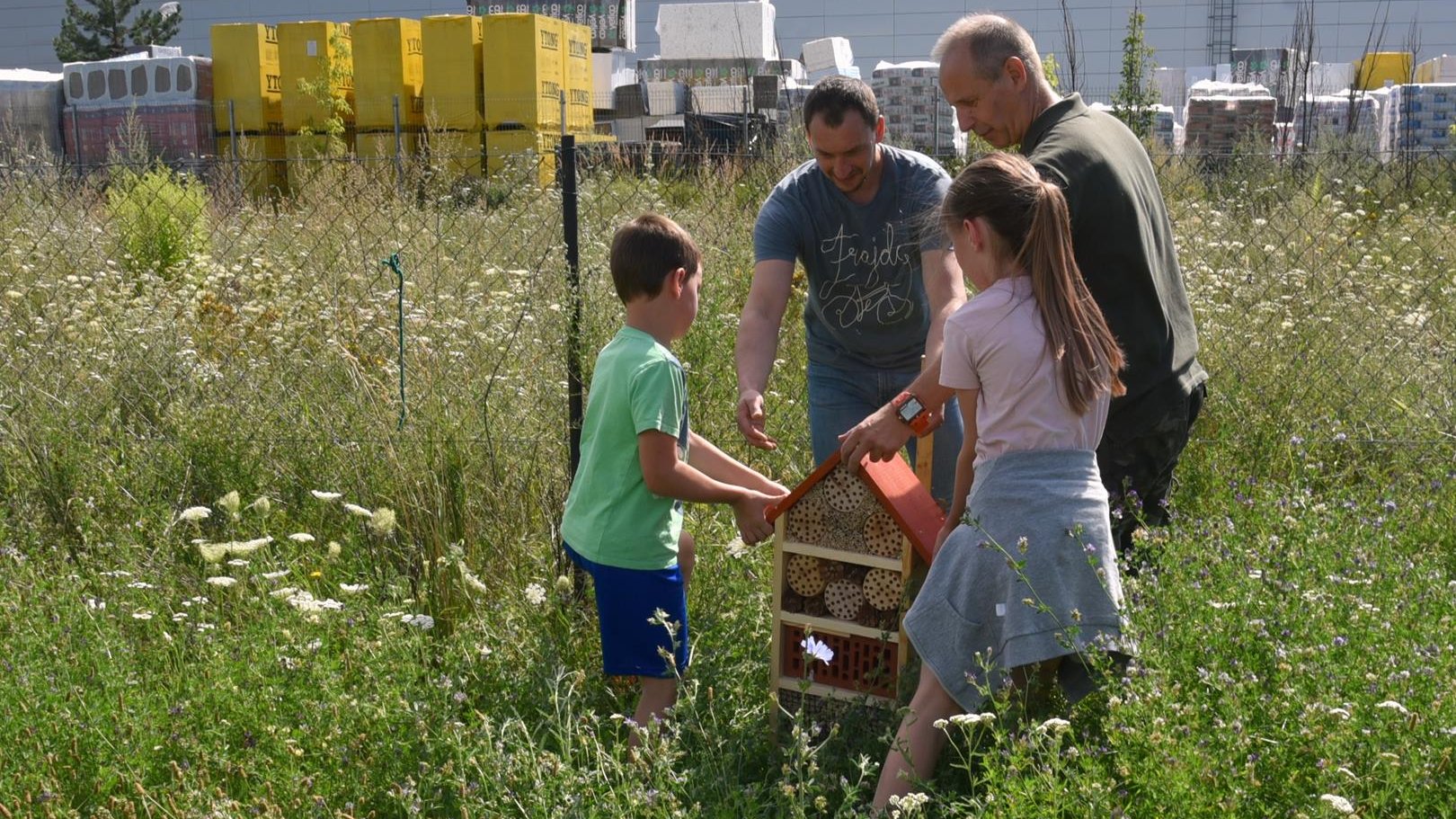 Dwóch mężczyzn montuje dom dla owadów, pomaga im dwoje dzieci, chłopiec i dziewczynka