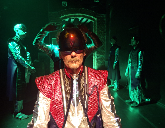 Z okazji przypadającego w tym roku 1000-lecia koronacji Bolesława Chrobrego i Mieszka II Lamberta, Teatr Usta Usta Republika zaprasza na spektakl "Plemię"/ fot. Teatr Usta Usta Republika Zdjęcie przedstawia mężczyznę w średniowiecznym stroju z dziwnym kaskiem na głowie. W tle widać innych mężczyzn.
