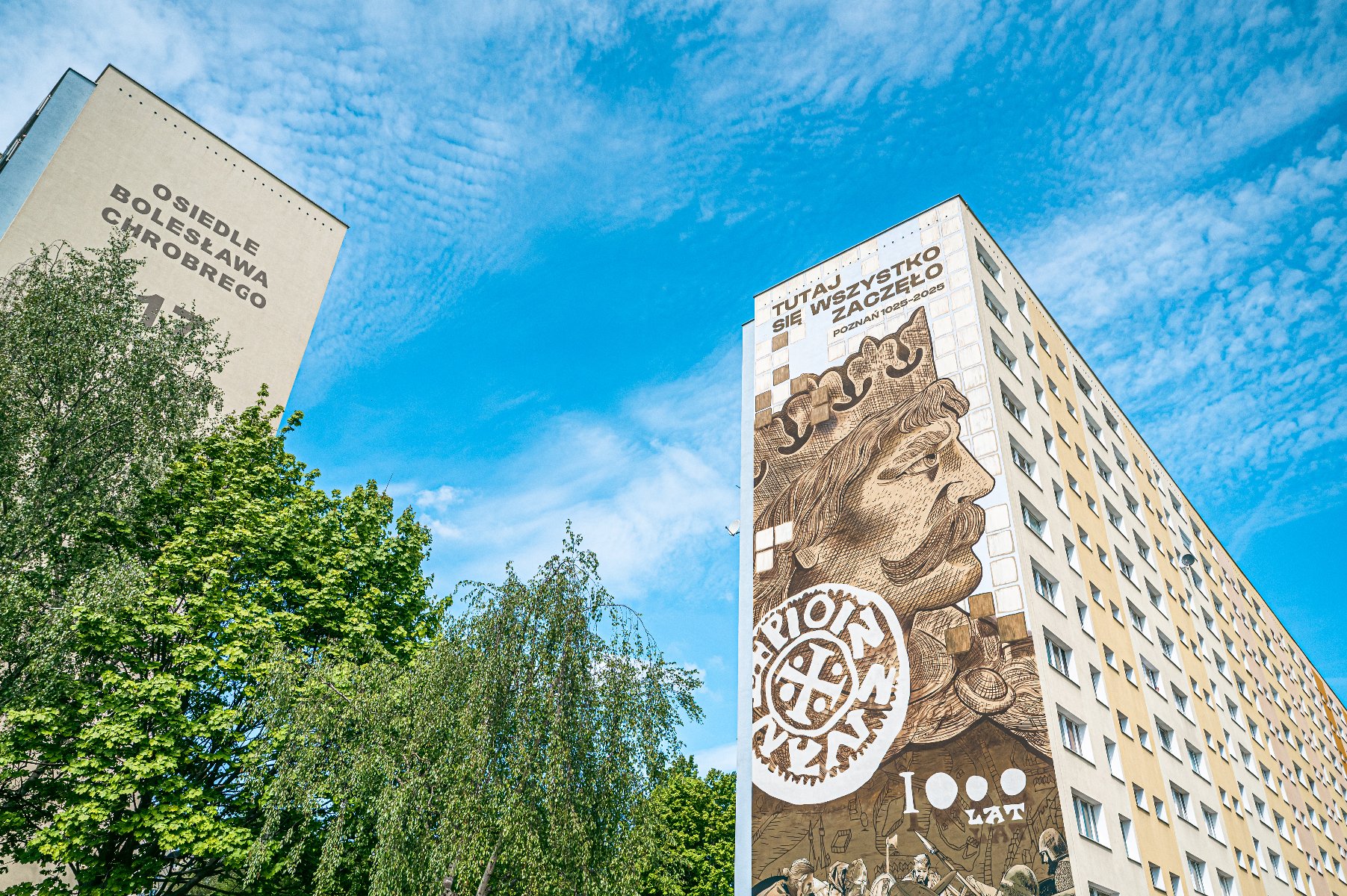 Można już podziwiać mural upamiętniający rocznicę 1000-lecia koronacji Bolesława Chrobrego Zdjęcie przedstawia mural z wizerunkiem Bolesława Chrobrego na ścianie bloku. Obok widać drzewa.