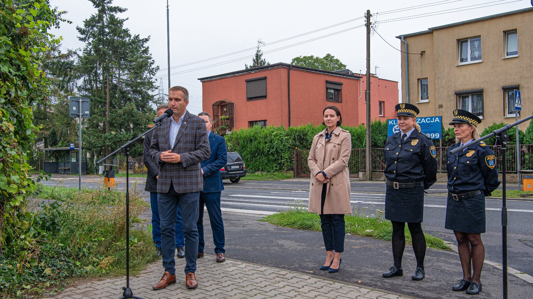 Zdjęcie z briefingu dotyczącego doświetleń przejść dla pieszych. Z przodu osoby mówiące na briefingu. W tle przejście, które będzie w tym roku doświetlone