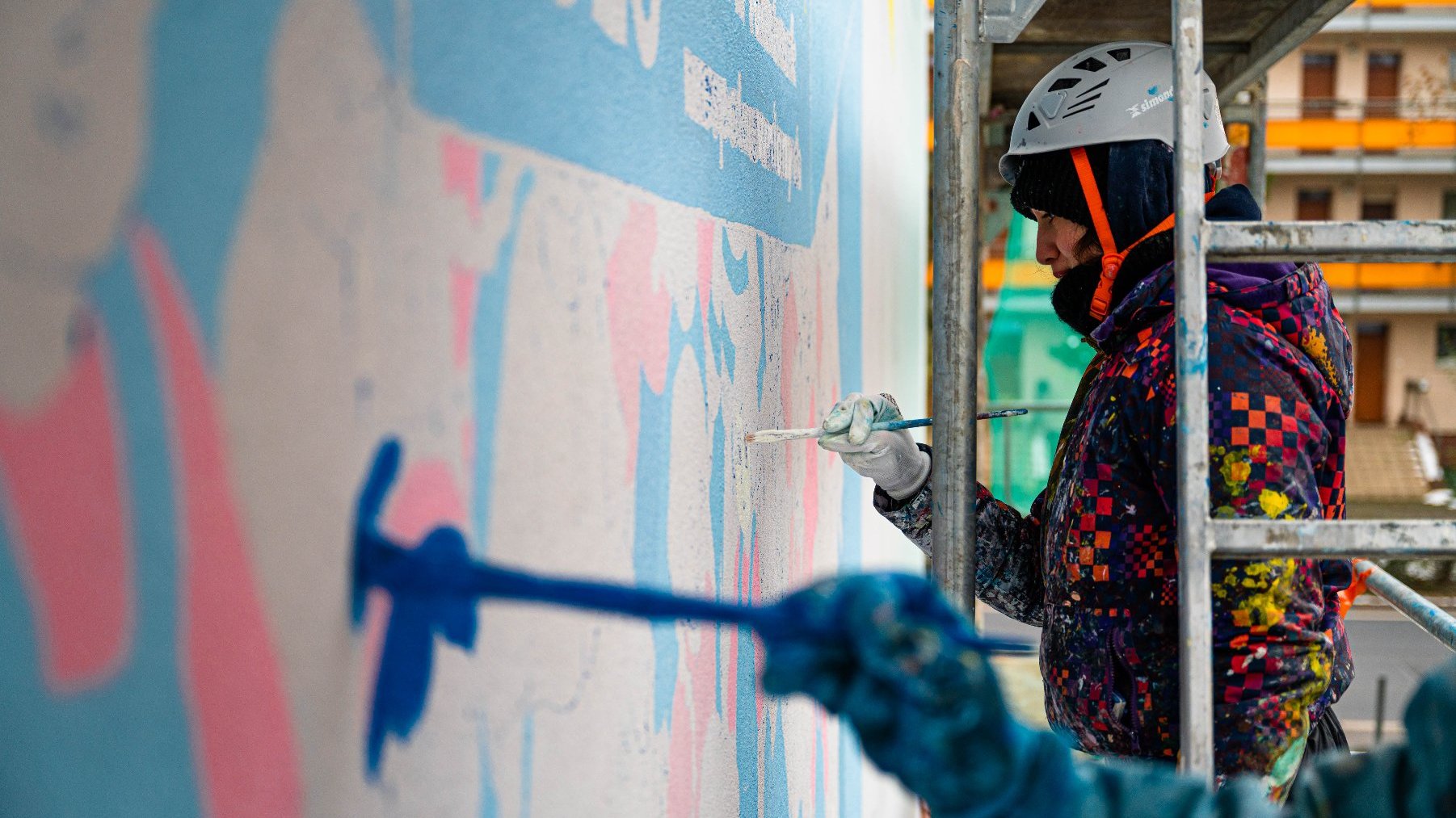 Na zdjęciu dwie kobiety na rusztowaniu, malujące mural