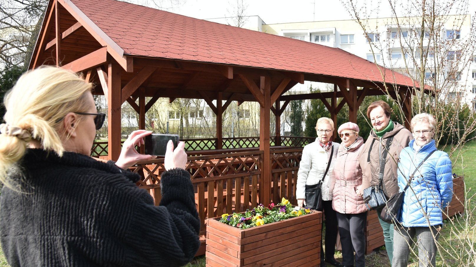 Zdjęcie przedstawia seniorów pozujących do zdjęcia na tle altany.