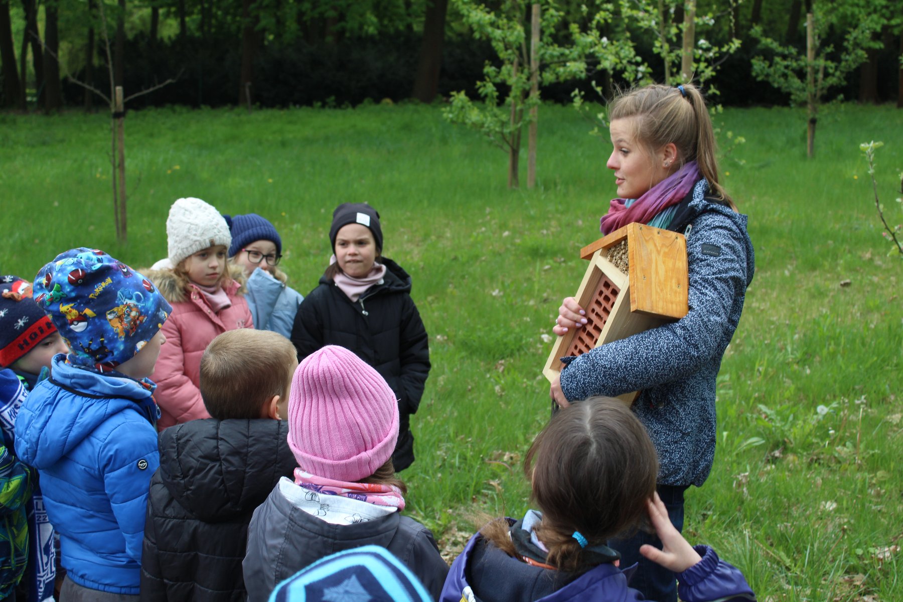 Zdjęcie przedstawia grupę dzieci i kobietę trzymającą domek dla owadów. - grafika artykułu