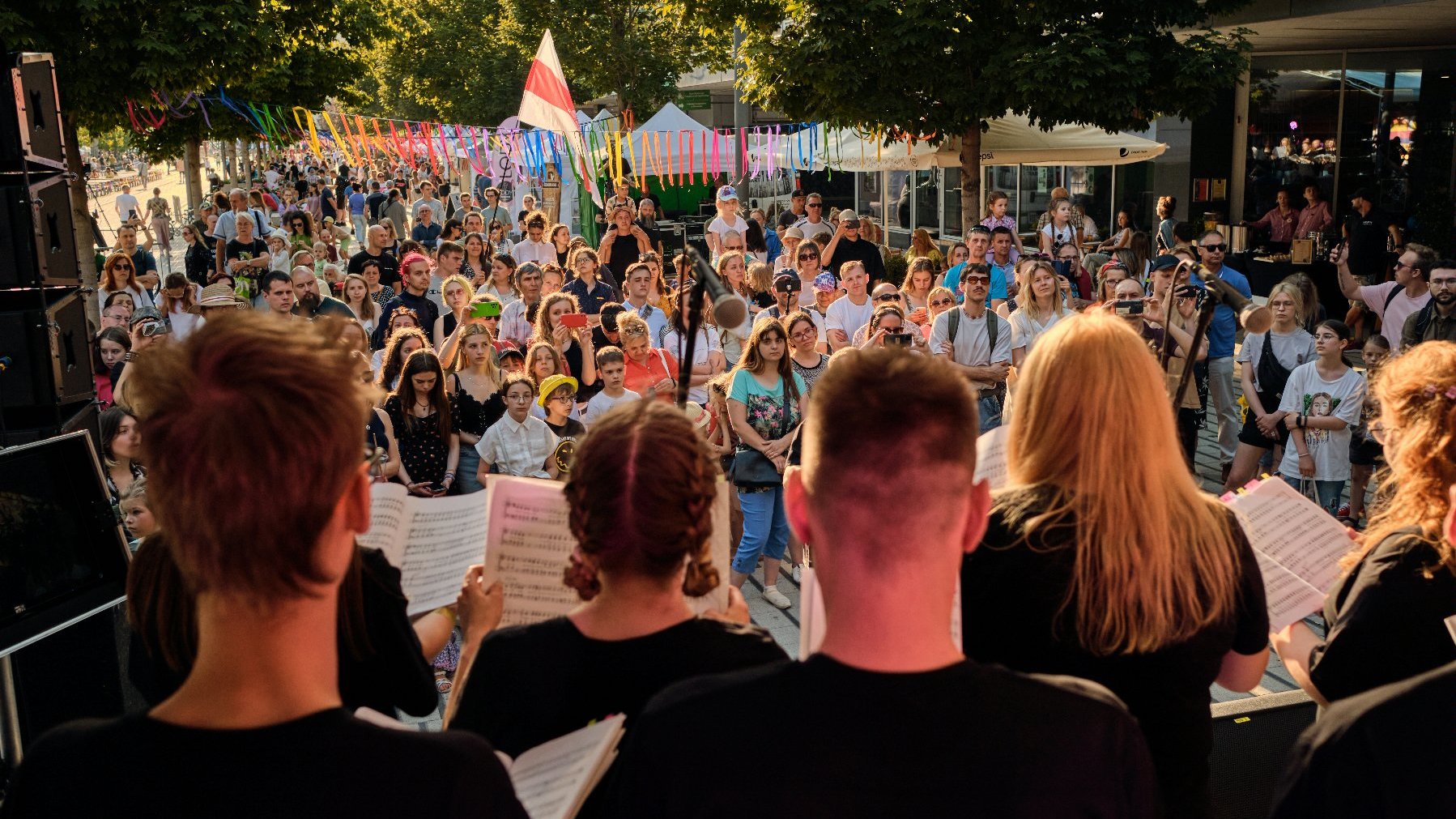 Na zdjęciu grupa śpiewających ludzi, przed nimi publiczność