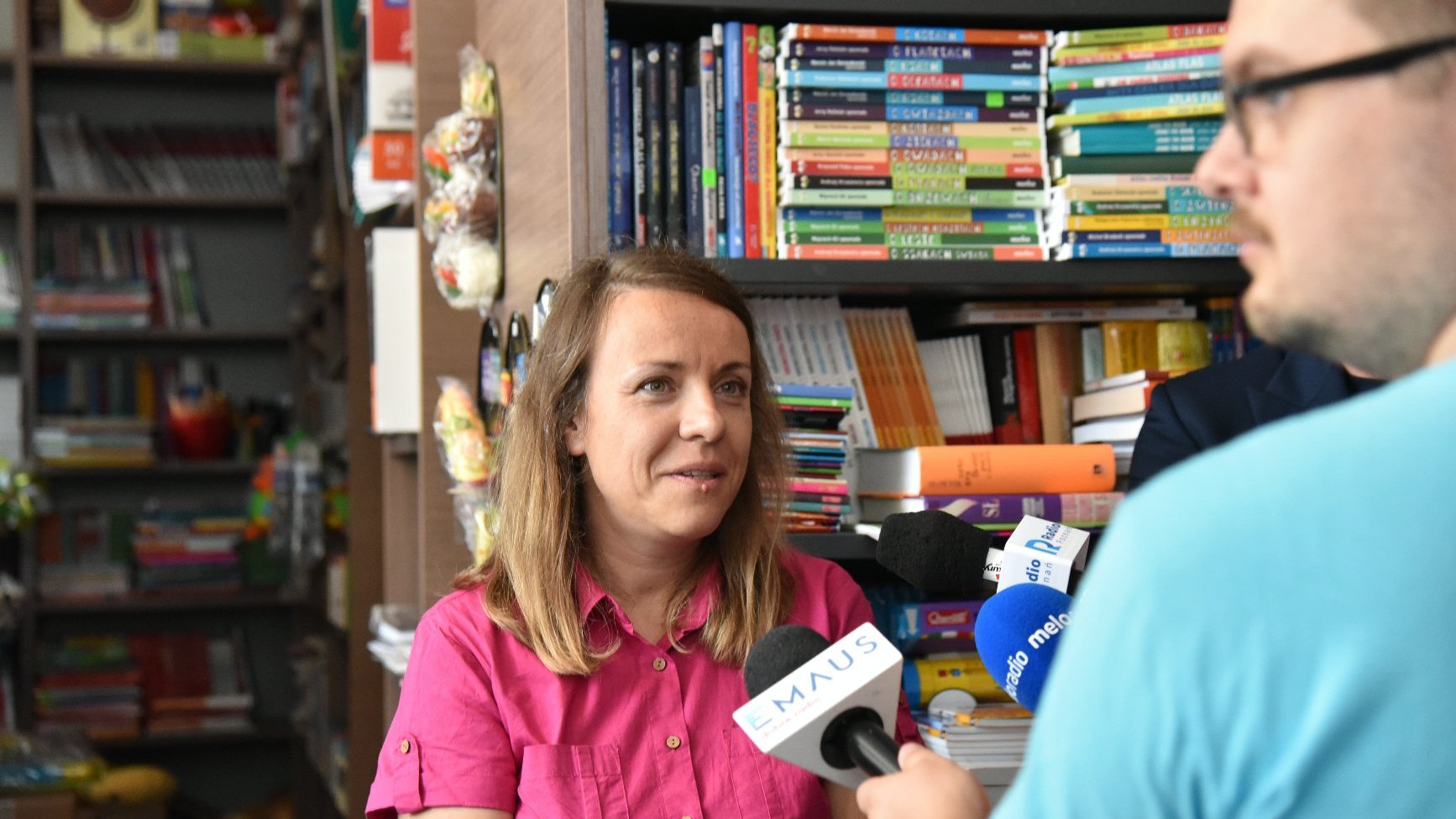 Zdjęcie przedstawia kobietę mówiącą do mikrofonu. Z tyłu widać półkę z książkami.