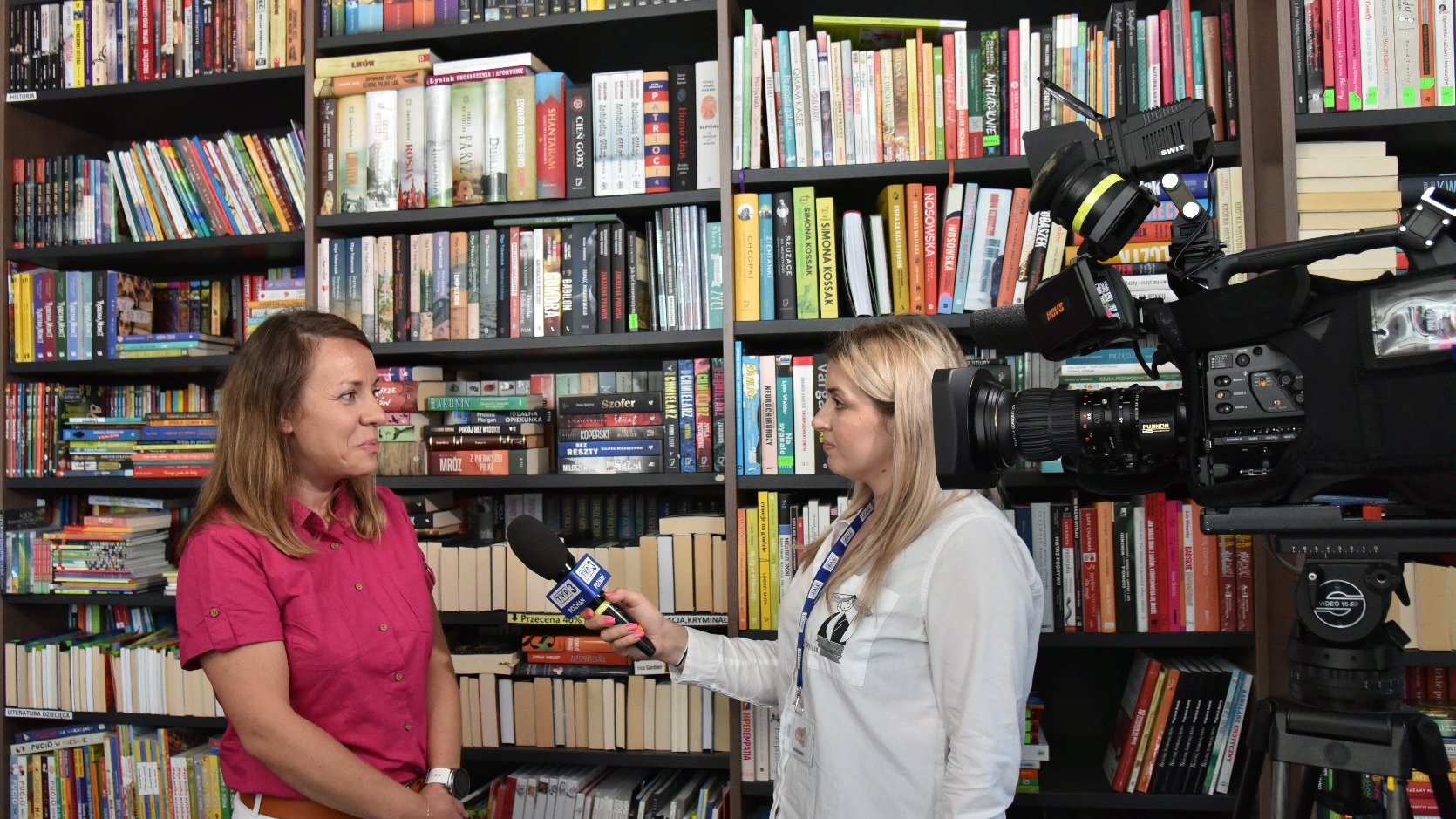 Zdjęcie przedstawia kobietę udzielającą wywiadu przed kamerą. Obok znajduje się półka z książkami.