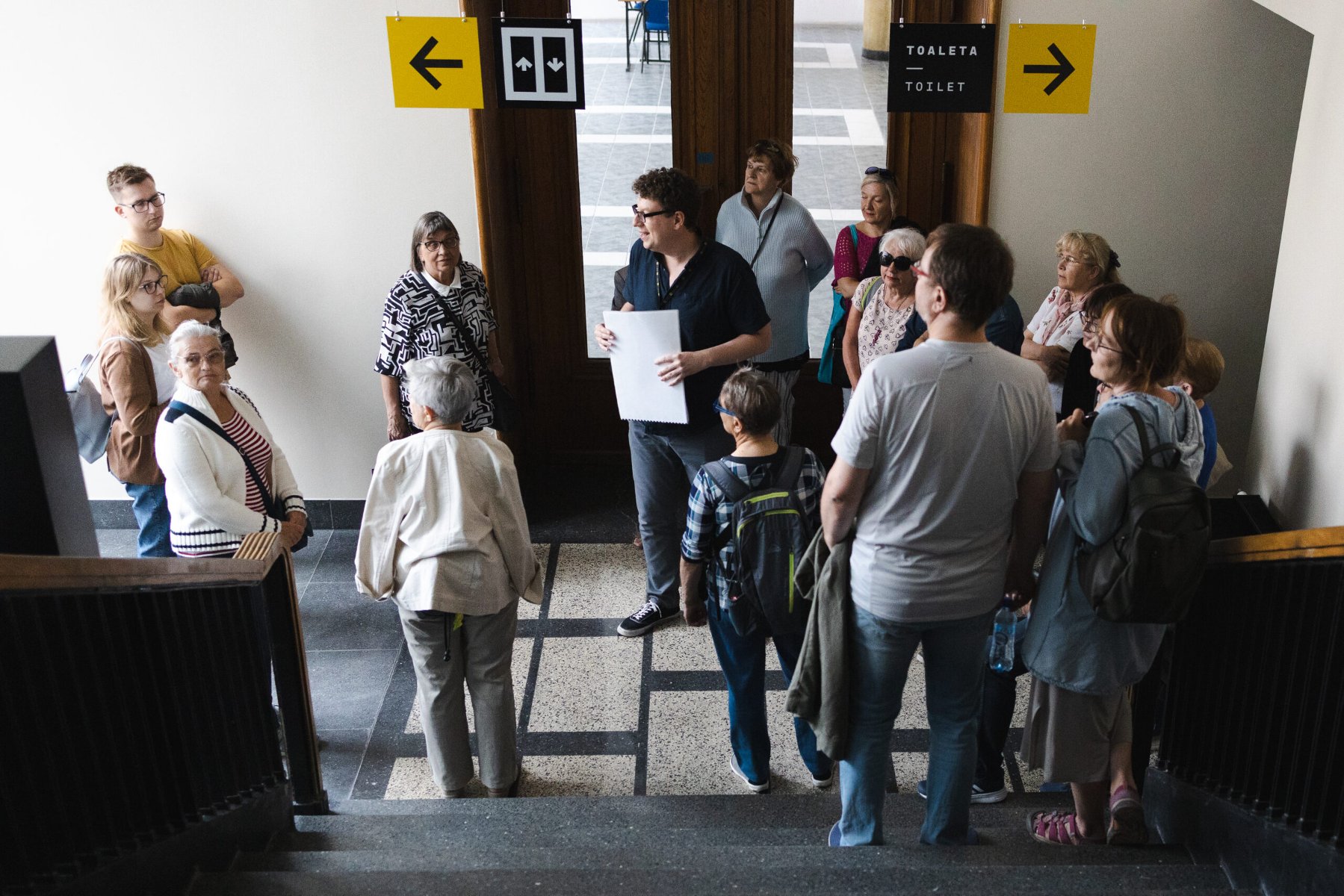 Uczestnicy wycieczki stoją na korytarzu Collegium Martineum i słuchają opowieści przewodnika. - grafika artykułu