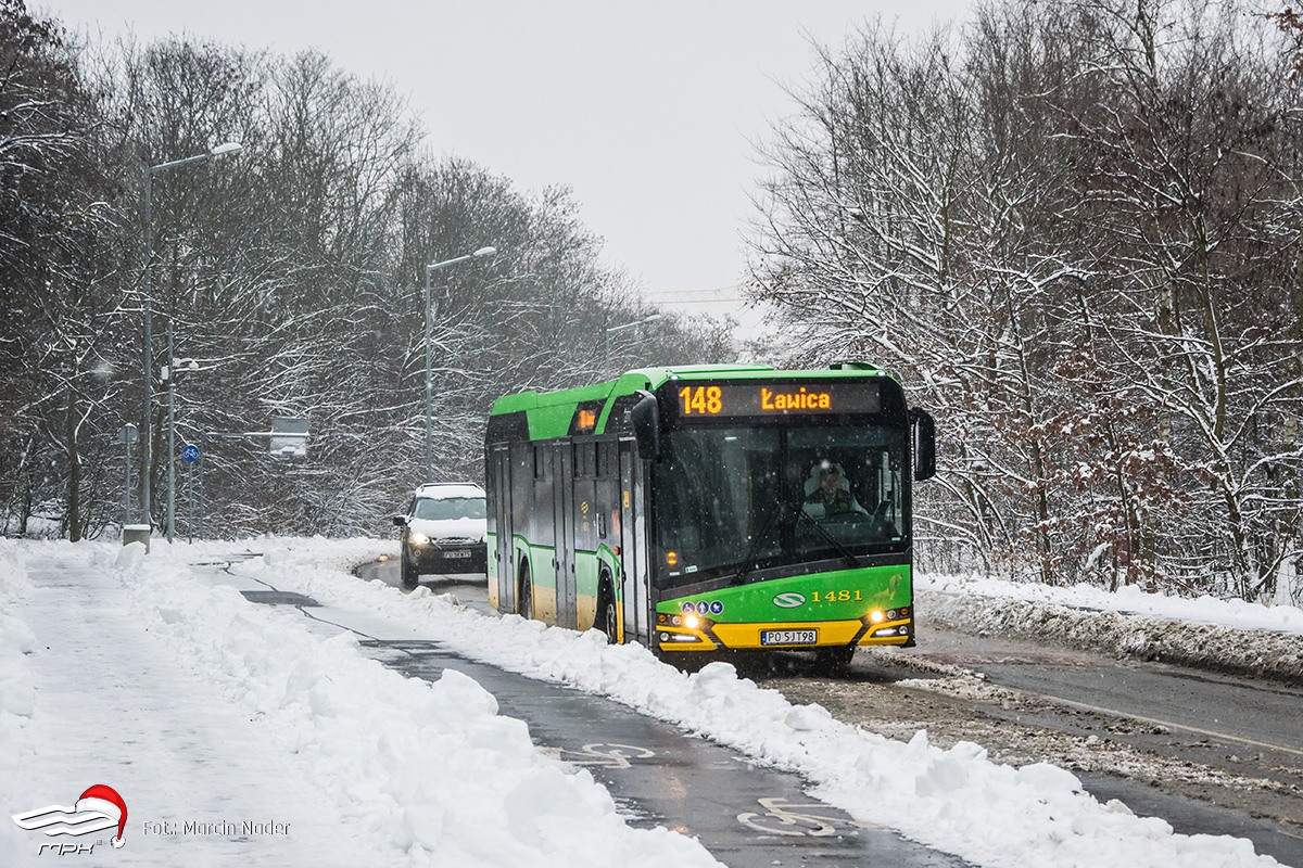 Zielono-żółty autobus jedzie po zaśnieżonej ulicy. Za nim podażą czarny samochód. Pada śnieg. Wokół ośnieżone drzewa. - grafika artykułu