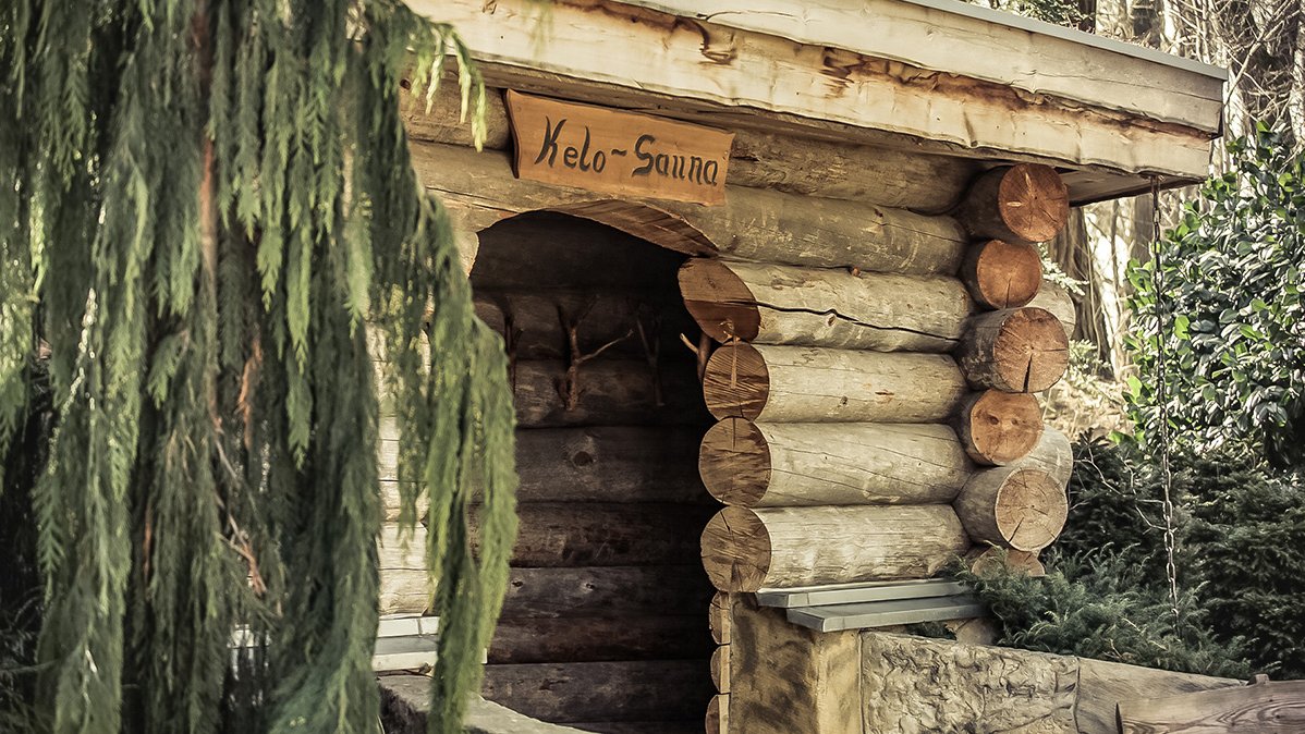 Drewniana konstrukcja przyminająca chatkę. Nad wejściem tabliczka "Kelo-Sauna". Dookoła egzotyczne rośliny.